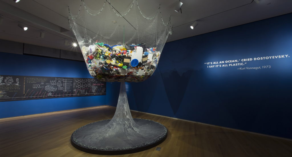 Photo credits: (Top) Crochet Coral Reef: TOXIC SEAS, by Margaret and Christine Wertheim and the Institute For Figuring, at Museum of Arts and Design, NY 2016. (Bottom) The Midden, four years worth of the Wertheim's domestic plastic trash. [Photos by Jenna Bascom courtesy of MAD.]